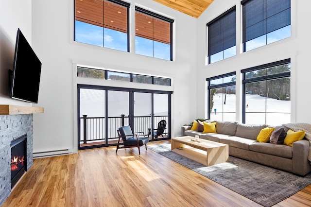 living area featuring a stone fireplace, baseboard heating, and wood finished floors