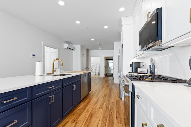 kitchen with blue cabinetry, a sink, white cabinetry, stainless steel appliances, and light wood-style floors