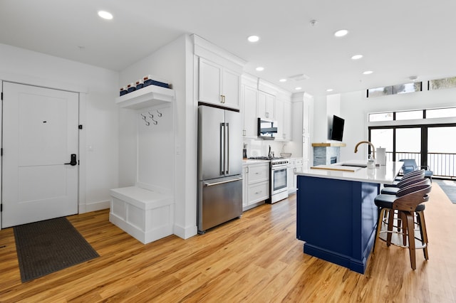 kitchen with light wood finished floors, high quality appliances, light countertops, white cabinets, and a sink