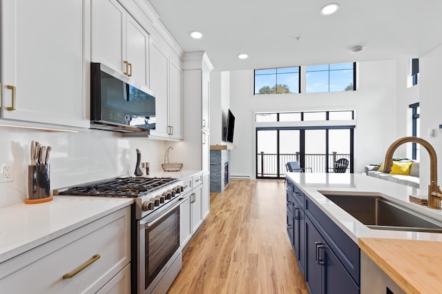 kitchen with gas stove, blue cabinetry, a fireplace, a sink, and white cabinetry