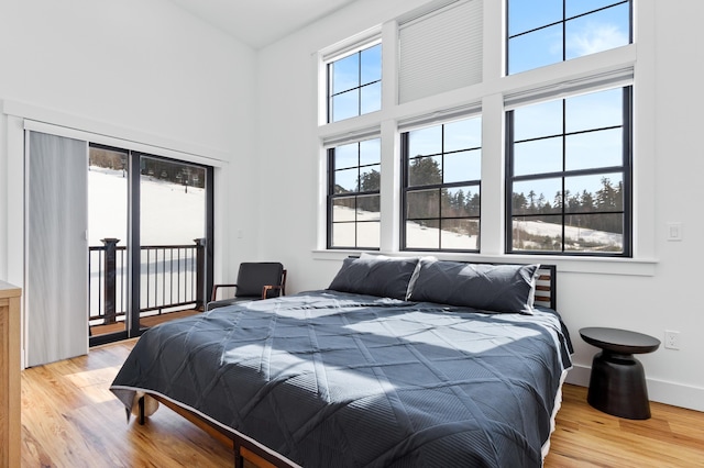 bedroom with access to outside, light wood-style flooring, baseboards, and a towering ceiling