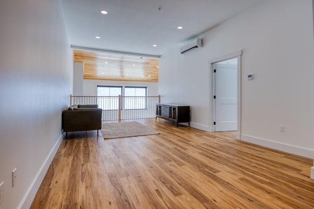 unfurnished living room with a wall unit AC, recessed lighting, baseboards, and light wood finished floors