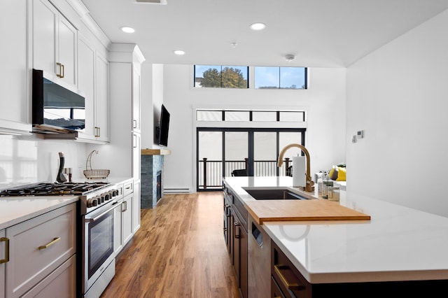 kitchen with gas stove, a center island with sink, a fireplace, a sink, and light wood-type flooring