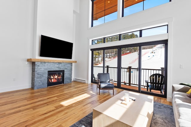 living area featuring a baseboard radiator, a fireplace, baseboards, and wood finished floors