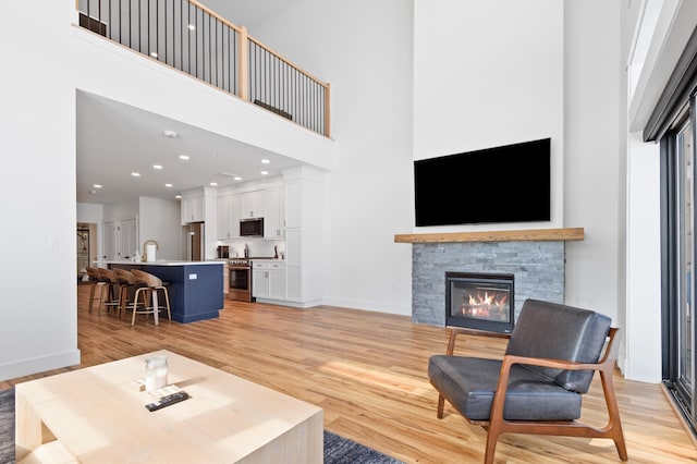 living room with light wood-style flooring, a fireplace, baseboards, and a towering ceiling