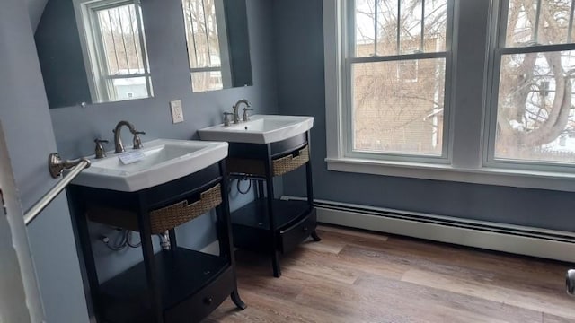 bathroom featuring a sink, a baseboard heating unit, a healthy amount of sunlight, and wood finished floors