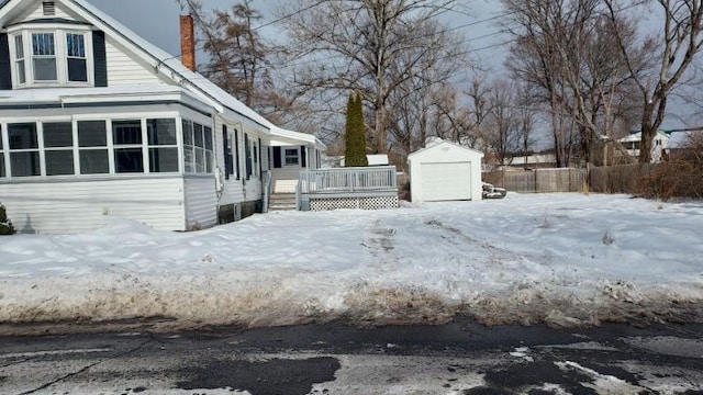 view of snow covered exterior with an outbuilding, a deck, fence, a garage, and a chimney