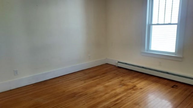 unfurnished room featuring a baseboard heating unit, baseboards, and light wood finished floors