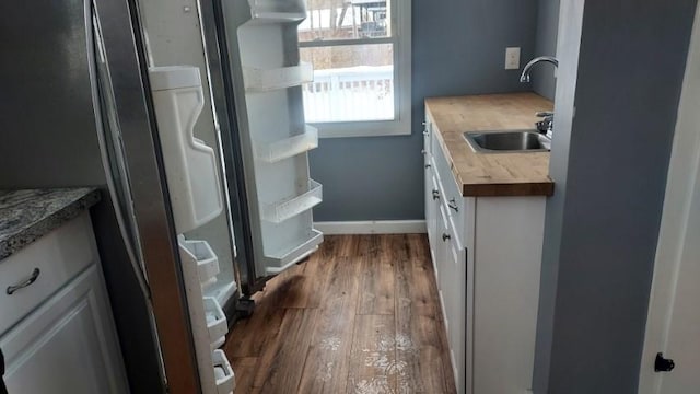 kitchen featuring white cabinetry, dark wood-style floors, baseboards, and a sink