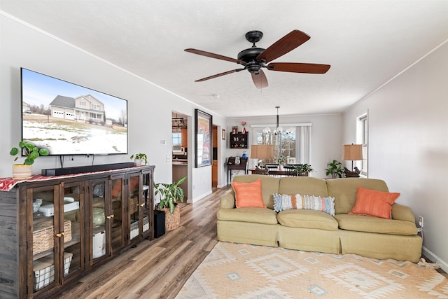 living room featuring baseboards, wood finished floors, crown molding, and ceiling fan with notable chandelier