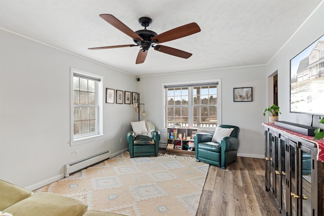 living area featuring a baseboard heating unit, ceiling fan, baseboards, ornamental molding, and light wood-style floors