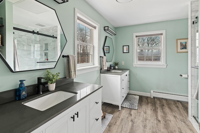 bathroom featuring a sink, baseboard heating, two vanities, and a shower stall