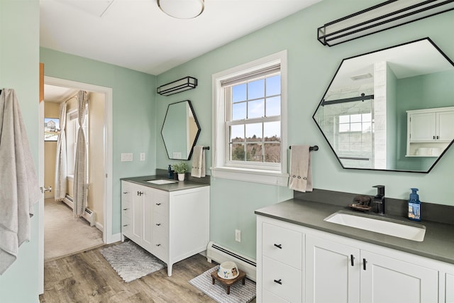 bathroom featuring wood finished floors, two vanities, a sink, a shower, and baseboard heating