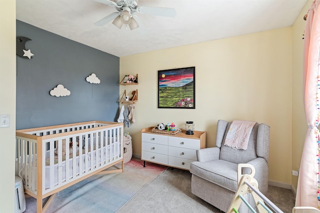 carpeted bedroom with baseboards, a crib, and ceiling fan