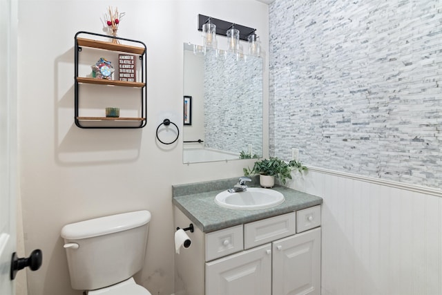 half bath featuring vanity, toilet, and a wainscoted wall