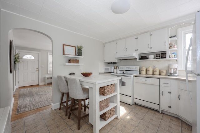 kitchen featuring arched walkways, white appliances, radiator heating unit, and open shelves