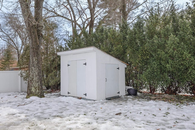 snow covered structure with fence, an outdoor structure, and a shed