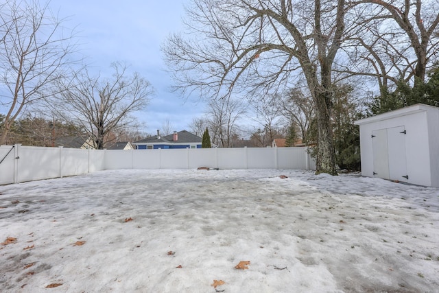 yard covered in snow featuring an outbuilding, a fenced backyard, and a shed