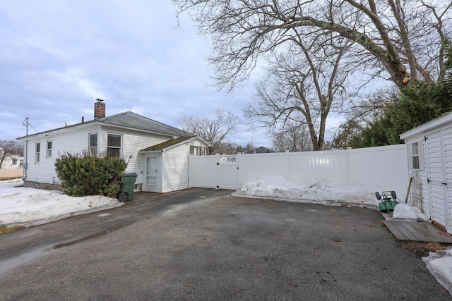 view of side of home with a chimney, fence, and a gate