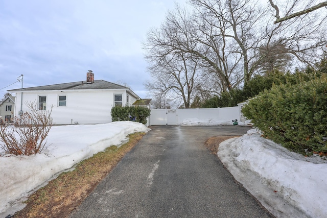 view of side of property with fence, a chimney, driveway, and a gate