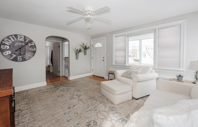 living room featuring arched walkways, baseboards, ceiling fan, and wood finished floors