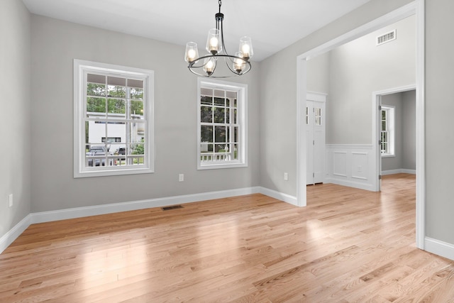 empty room featuring baseboards, visible vents, light wood finished floors, and a chandelier