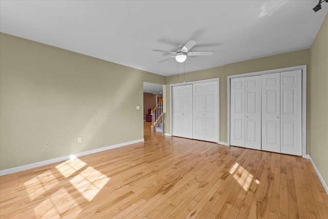 unfurnished bedroom with baseboards, two closets, and light wood-style floors