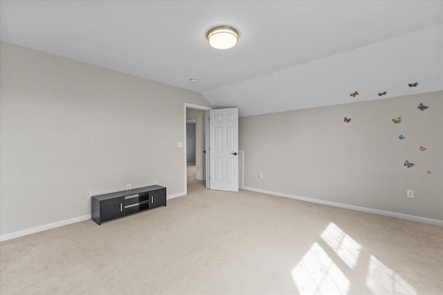 empty room with light colored carpet, baseboards, and vaulted ceiling