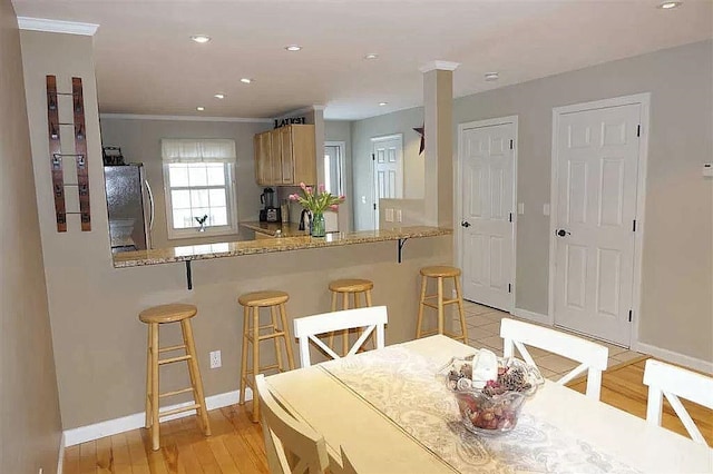 kitchen with light wood-type flooring, baseboards, a breakfast bar, and freestanding refrigerator