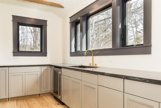 kitchen featuring wine cooler, lofted ceiling with beams, light wood-type flooring, dark stone countertops, and a sink