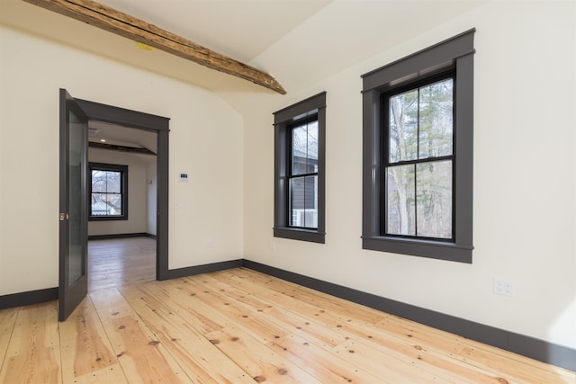 spare room featuring lofted ceiling with beams, light wood-type flooring, and baseboards