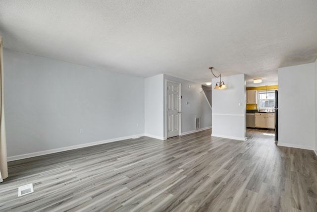 unfurnished living room featuring visible vents, baseboards, a textured ceiling, and wood finished floors