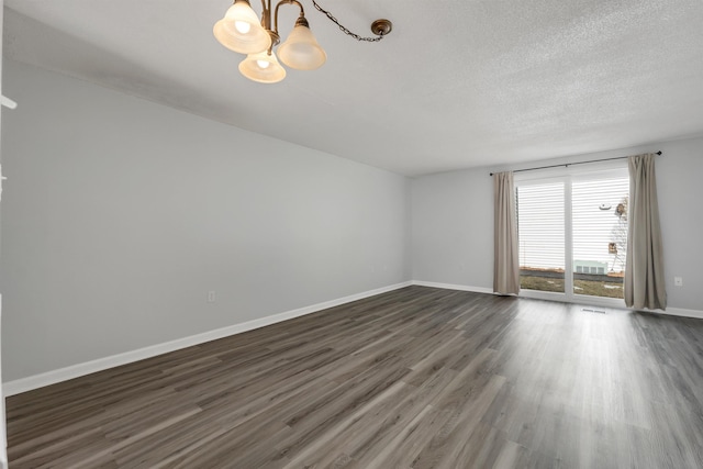 unfurnished room with a chandelier, dark wood-style floors, a textured ceiling, and baseboards