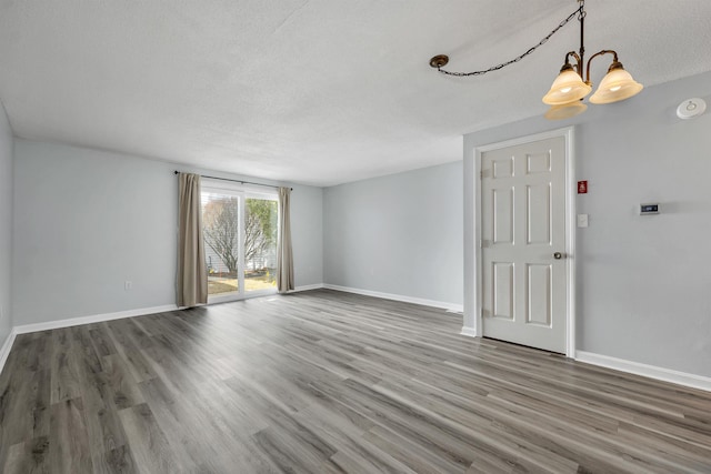 unfurnished room featuring a notable chandelier, a textured ceiling, baseboards, and wood finished floors