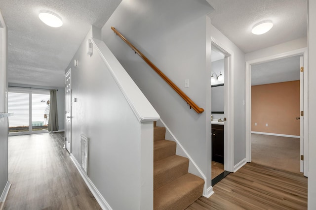 stairs featuring visible vents, wood finished floors, baseboards, and a textured ceiling