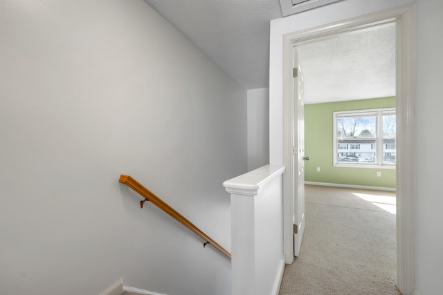 staircase featuring a textured ceiling, baseboards, and carpet