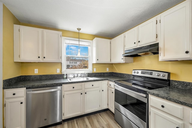 kitchen with under cabinet range hood, stainless steel appliances, dark countertops, and a sink