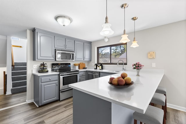 kitchen featuring a peninsula, gray cabinets, a sink, stainless steel appliances, and a kitchen breakfast bar