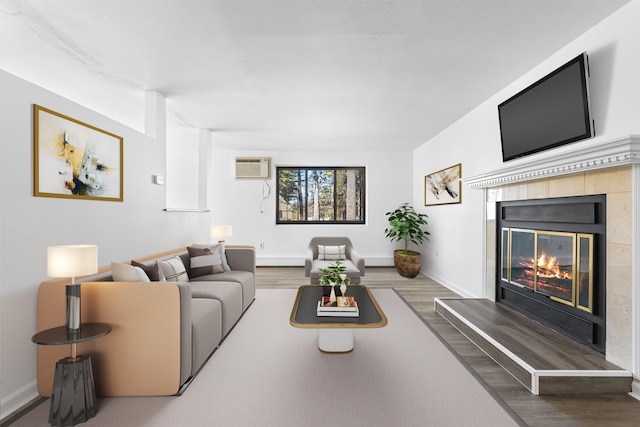 living area featuring a tiled fireplace, wood finished floors, baseboards, and a wall mounted AC