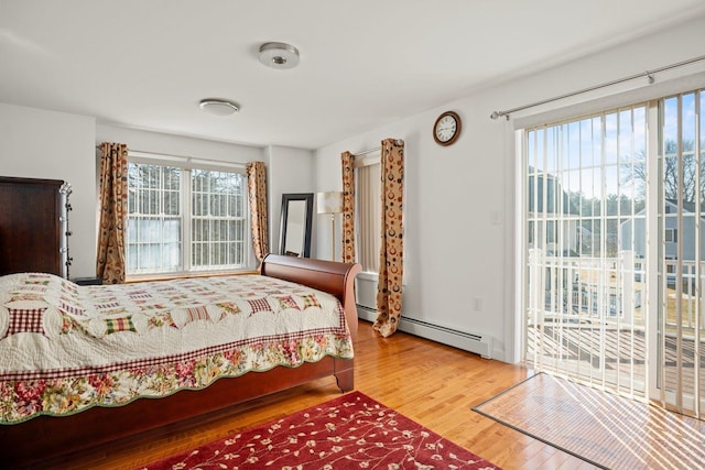 bedroom featuring multiple windows, baseboard heating, wood finished floors, and access to outside