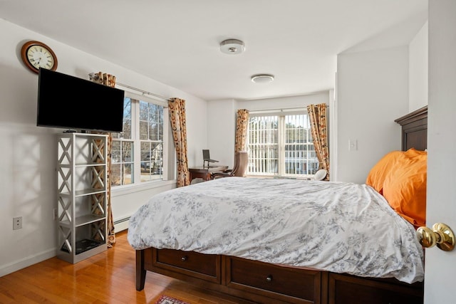 bedroom with light wood-type flooring, baseboards, a baseboard heating unit, and access to outside