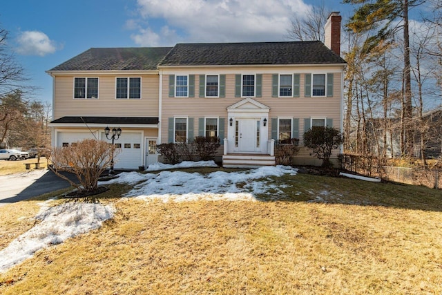 colonial-style house featuring an attached garage, a chimney, driveway, and a shingled roof