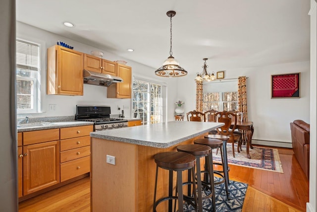 kitchen featuring light wood finished floors, a kitchen island, under cabinet range hood, range with gas stovetop, and baseboard heating