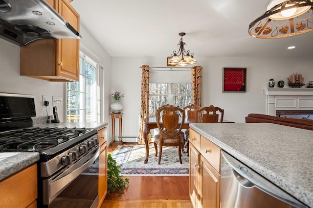 kitchen featuring light countertops, under cabinet range hood, appliances with stainless steel finishes, a baseboard heating unit, and a chandelier