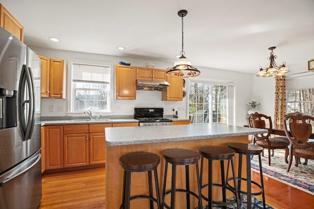 kitchen with light wood-style flooring, a sink, stove, under cabinet range hood, and stainless steel fridge