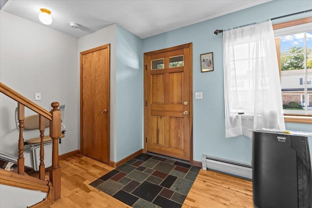 foyer featuring baseboard heating, stairway, baseboards, and wood finished floors