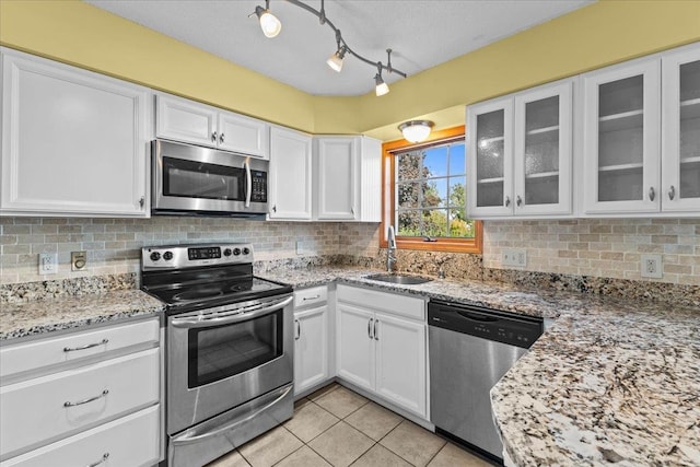 kitchen featuring light tile patterned flooring, a sink, stainless steel appliances, white cabinetry, and tasteful backsplash