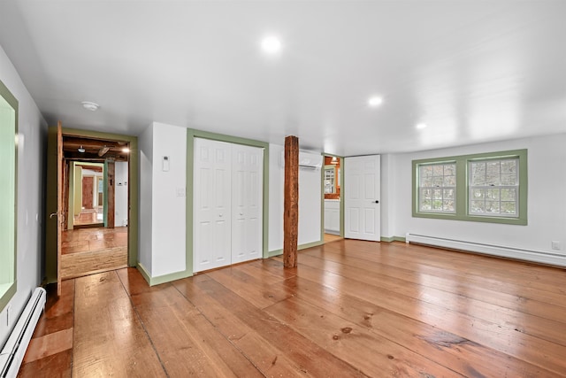 unfurnished bedroom with a baseboard heating unit, a wall mounted AC, and hardwood / wood-style flooring