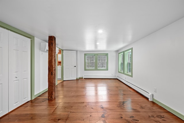 unfurnished bedroom featuring a baseboard heating unit, a wall mounted air conditioner, a closet, and hardwood / wood-style floors