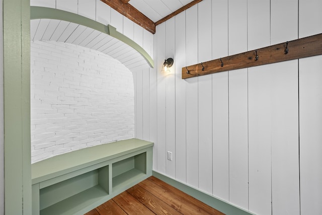 mudroom with beamed ceiling, wood finished floors, and brick wall